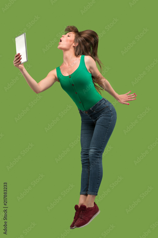 Image of young woman over green background using laptop computer or tablet gadget while jumping. Image of young woman over green background using laptop computer or tablet gadget while jumping.