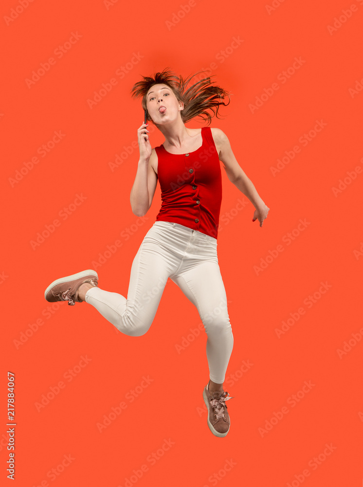 Full length of pretty young woman with mobile phone while jumping