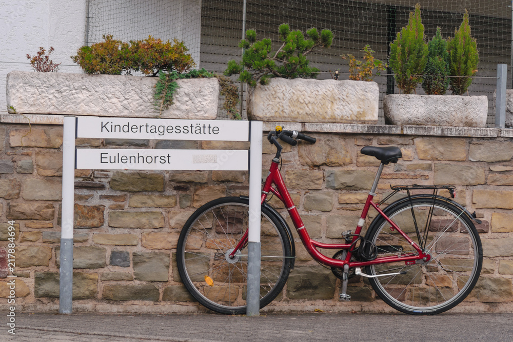 Red bike parked on a stone wall next to a street sign Red bike parked on a stone wall next to a street sign