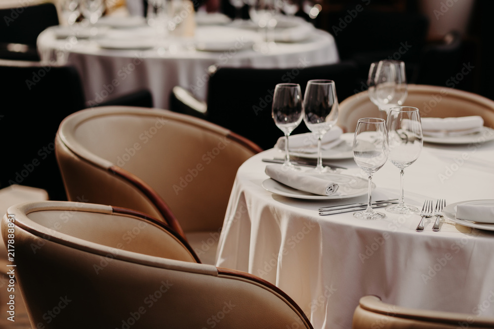 Horizontal shot of served round table with white tableclothes, wineglasses, plates, forks and knives, two armchairs near. Cozy atmosphere in luxury restaurant. Horizontal shot of served round table with white tableclothes, wineglasses, plates, forks and knives, two armchairs near. Cozy atmosphere in luxury restaurant.