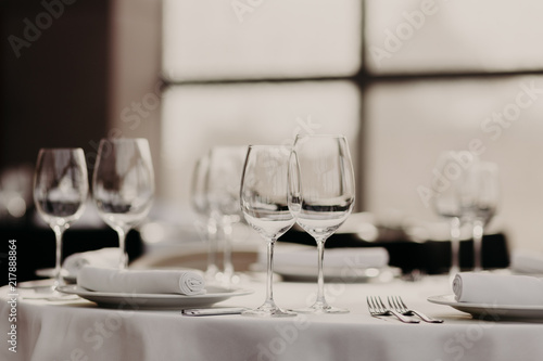 Catering and celebration concept. Festive served dinner table with glasses and cutlery on white tablewear in luxury banquet with no people. Table setting