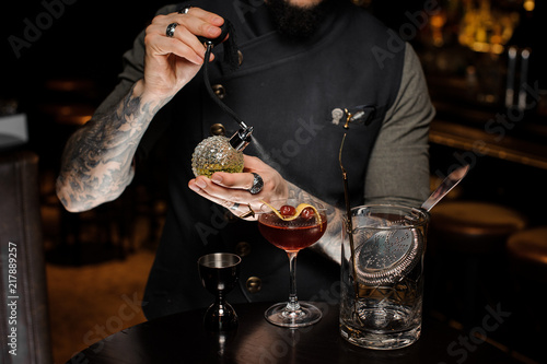 Barman with tattoo making a fresh and sweet summer cocktail with cherries