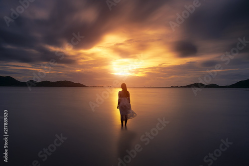 A lonely girl is walking along island coastline and has reflection on wet sand.