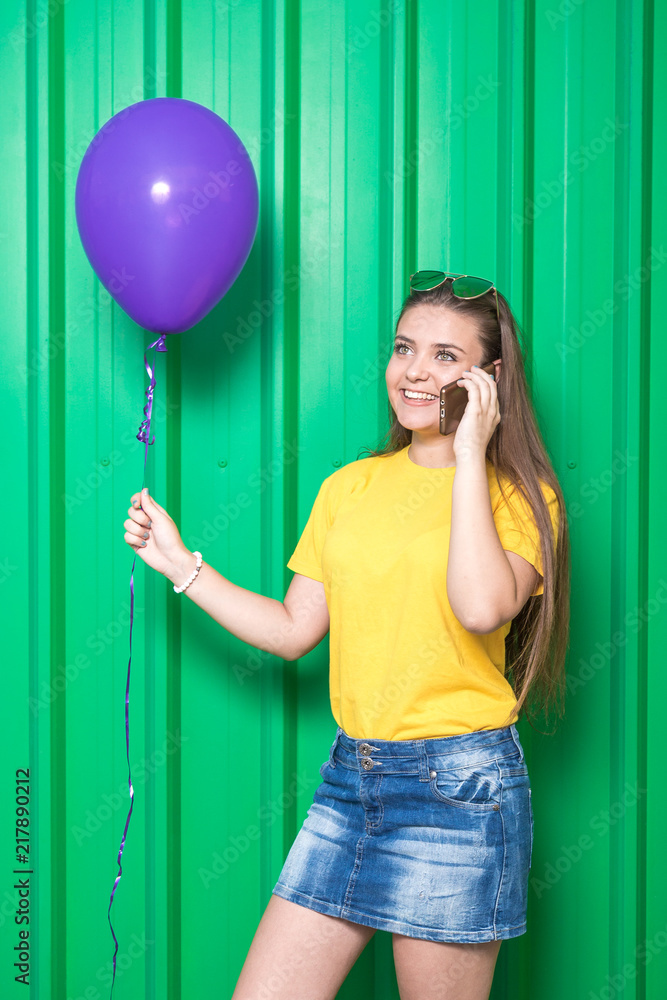 Φωτογραφία Portrait of girl with smartphone and balloon against green wall.