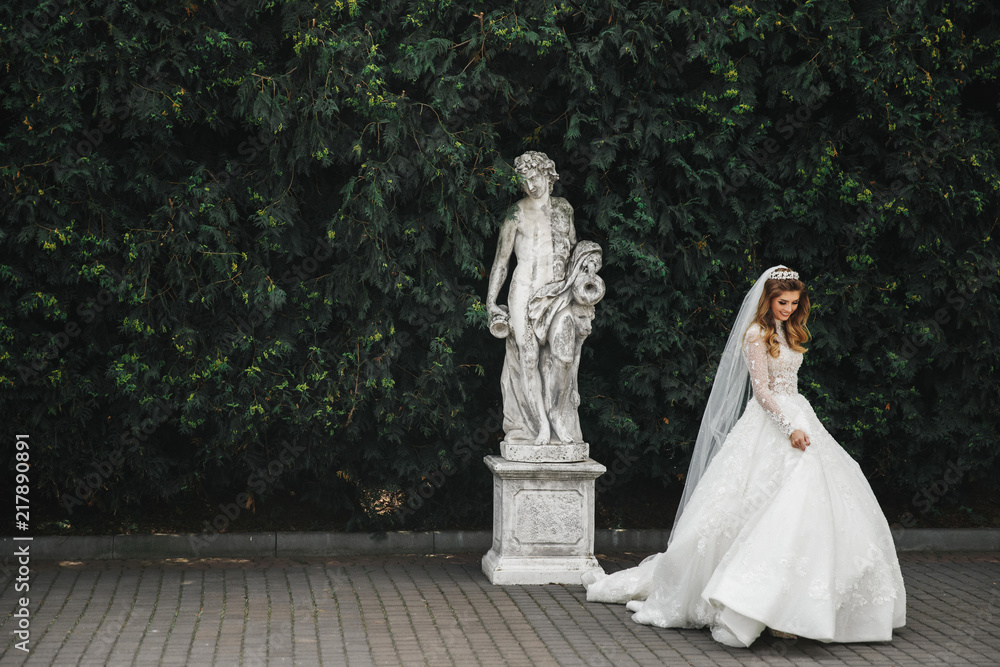 Charming bride poses before an antique statiue in the garden