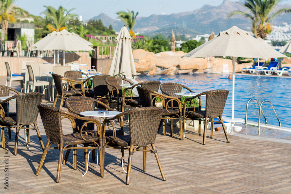 A cozy restaurant by the pool with wicker chairs and tables under the open sky.