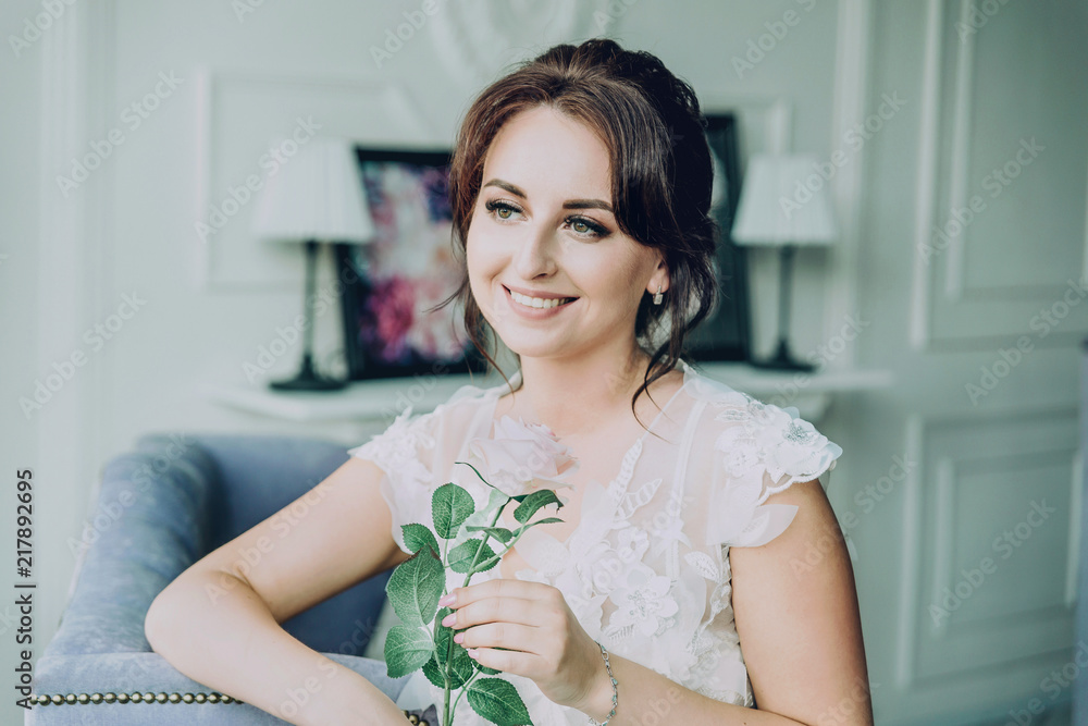 Portrait of a beautiful bride in a white negligee. She smiles and holds a rose in her hands. Portrait of a beautiful bride in a white negligee. She smiles and holds a rose in her hands.