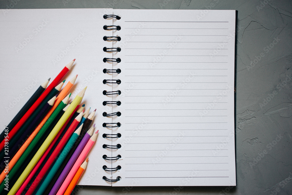 multicolored pencils, textbook, on gray plastered background, copy space multicolored pencils, textbook, on gray plastered background, copy space