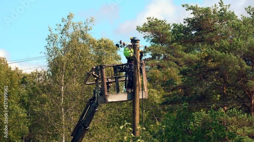 Electrical worker in an safety jumpsuit and hard hat repairs a problem on the power line in the forest, part 2 of 3
