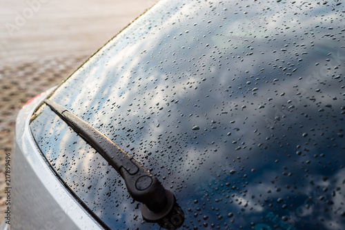 Fotografia Raindrops on a silver car on the rear black window of the car with visible rear wiper