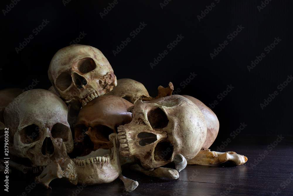 Pile of skulls and bones put on dark wooden plank which has dim light and the dark wall background Pile of skulls and bones put on dark wooden plank which has dim light and the dark wall background