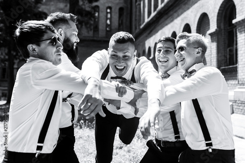 Groomsmen hold groom on their arms standing on the backyard in a sunny day