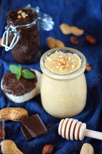 White and chocolate peanut urbech in glass jars surrounded by the ingredients. Top view photo