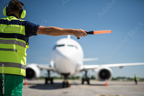 Important signal. Back view of airport worker meeting aircraft and showing right position for landing photo