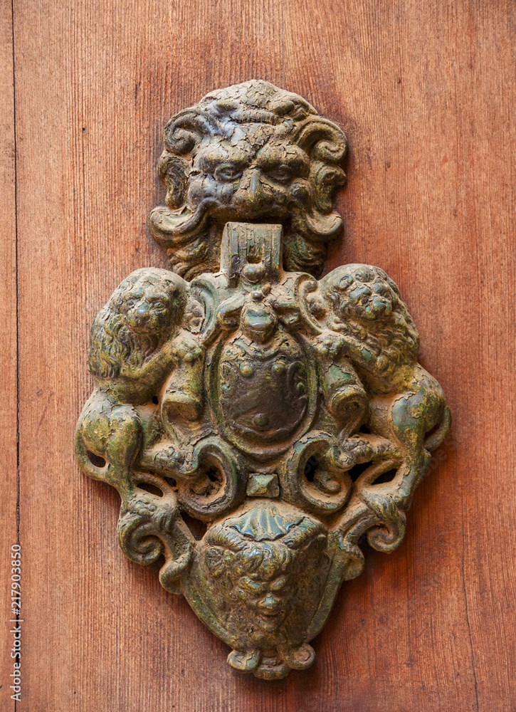Very old door clapper with emblem between two lions, monstrous face and rust on a wooden door Very old door clapper with emblem between two lions, monstrous face and rust on a wooden door