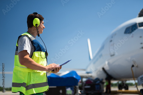 Checking the jet. Side view of airport crew member. Man wearing headphones and holding the clipboard