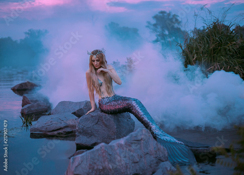 Canvastavla a beautiful mermaid is sitting on the rock in the purple fog