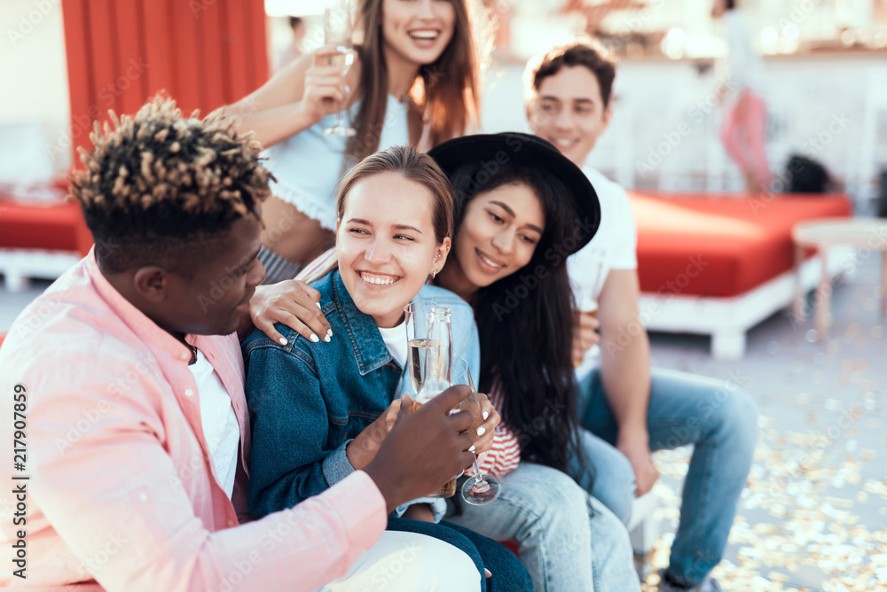 Fototapeta premium Happy girls talking with outgoing males while resting on comfortable couch outside. They tasting beverage