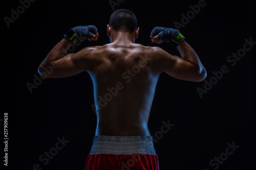 Rear view of strong young male boxer. Fitness male model wearing boxing gloves standing on black background. © nazarovsergey