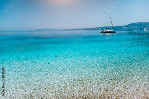 Fototapeta Naklejka Na Ścianę i Meble -  Sailing catamaran yacht boat at anchor near pebble beach with calm pure clear azure blue water surface