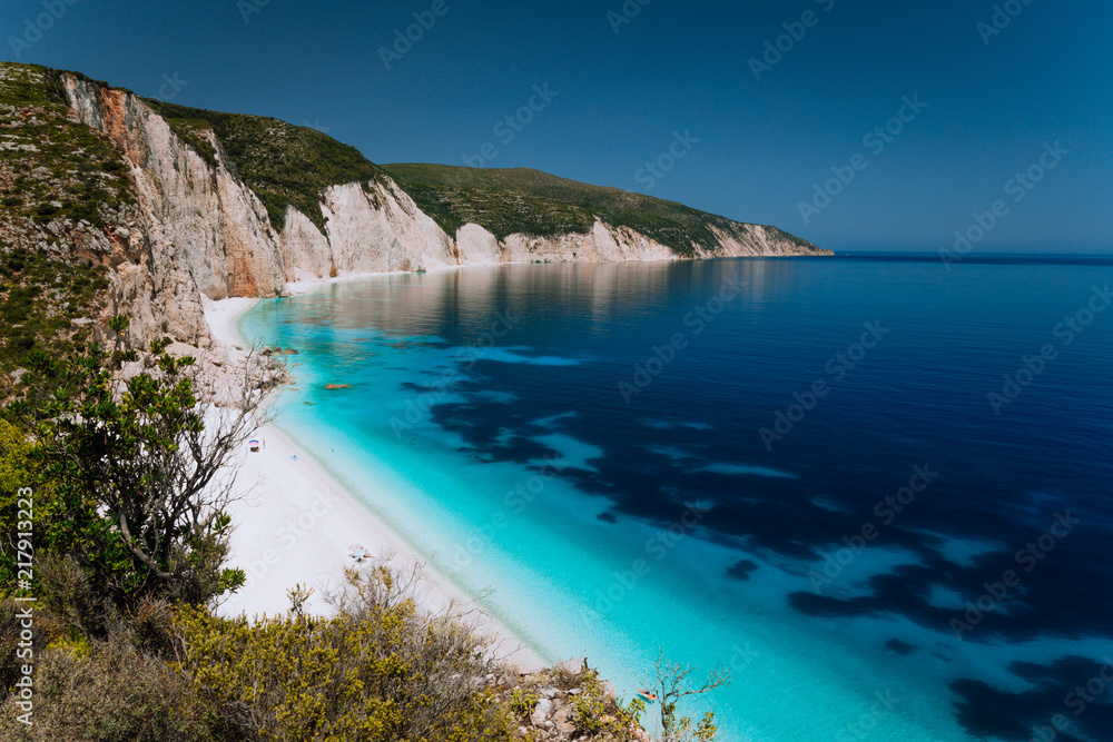 Panoramic view of Fteri beach, blue lagoon with rocky coastline, Kefalonia, Greece. Calm clear blue emerald green turquoise sea water with dark deep pattern