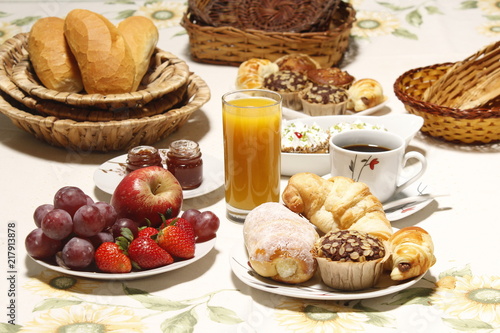 Mesa de café da manhã, com maçãs, morango, suco de laranja, pães, croissant e café.