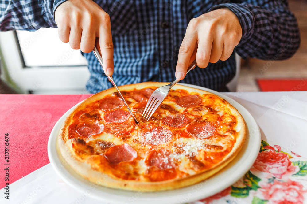 Happy hungry man eating pizza using fork and knife in italian restaurant