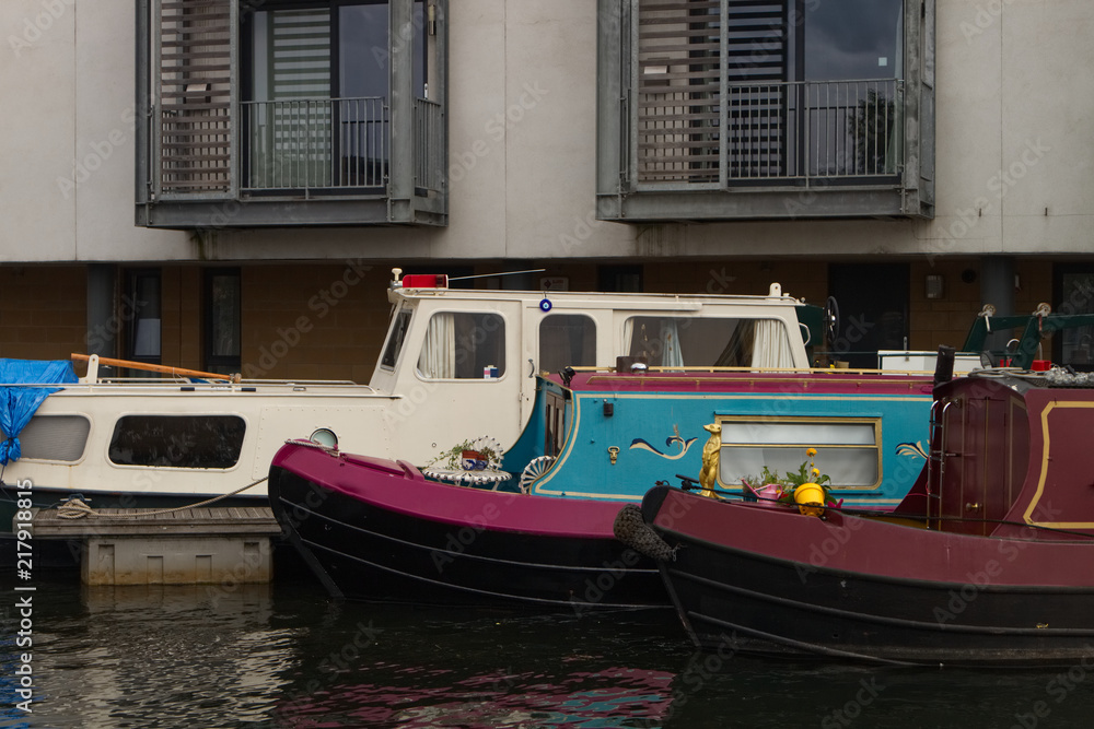 A photograph of three house boats or barges on canal in the United Kingdom docked next to residential flats