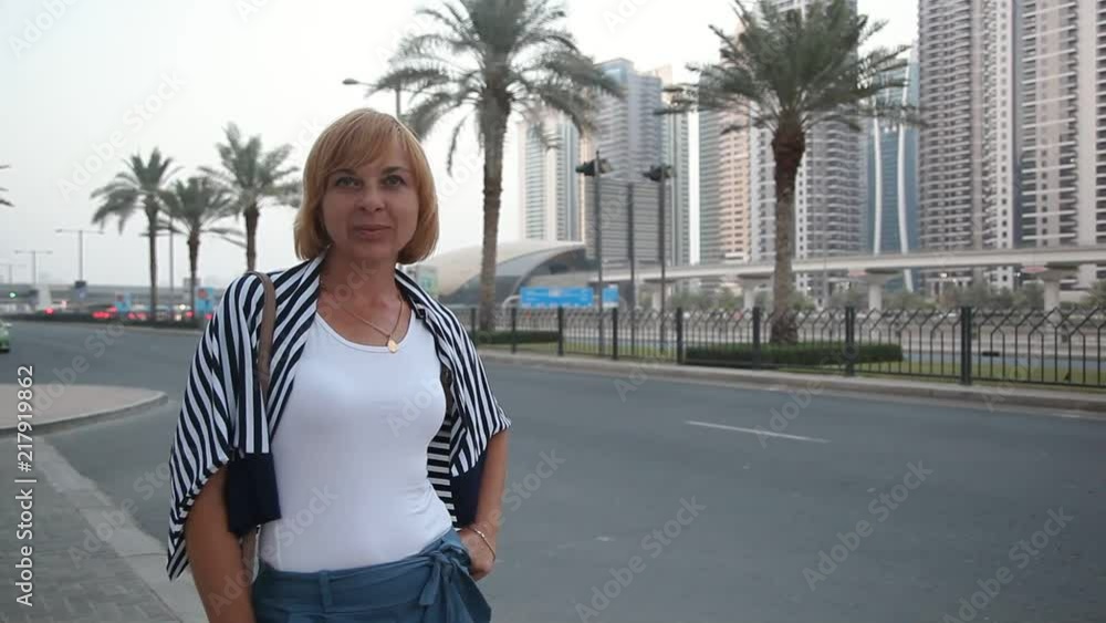 A cheerful view of an elegant woman standing and smiling happily at a modern highway with palms in Dubai on a sunny day in summer A cheerful view of an elegant woman standing and smiling happily at a modern highway with palms in Dubai on a sunny day in summer