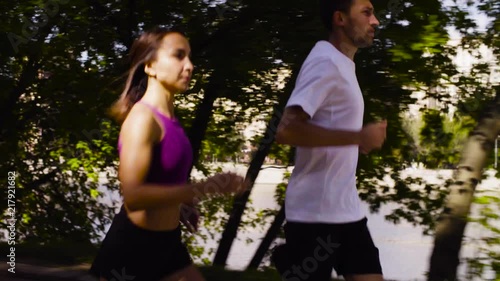 Dolly shot of young woman and man running in the city near the river. Side view