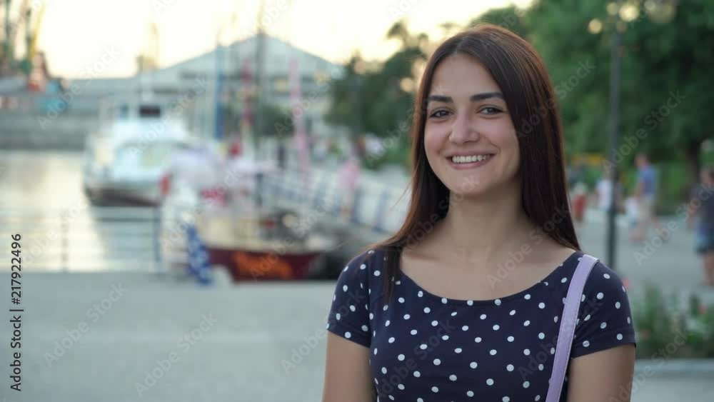 Portrait of an optimistic young woman in a polka-dot dress laughing and standing on a river embankment with yachts at a nice sunset in summer Portrait of an optimistic young woman in a polka-dot dress laughing and standing on a river embankment with yachts at a nice sunset in summer
