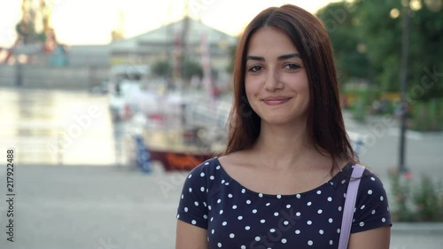 Portrait of a tender young woman with sparkling eyea in a polka-dot dress standing on a river quay with yachts at splendid sunset in summer   photo