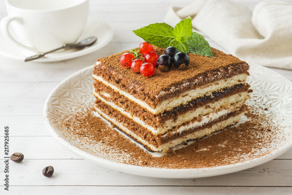 Delicious Tiramisu cake with fresh berries and mint on a plate on a light background. Breakfast with a Cup of coffee. Delicious Tiramisu cake with fresh berries and mint on a plate on a light background. Breakfast with a Cup of coffee.