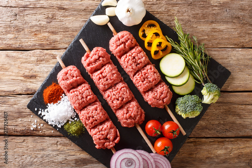 raw kebab of ground beef with ingredients and vegetables close-up.  Horizontal top view from above photo