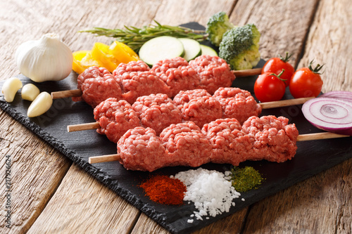 Homemade kebabs from raw minced meat on skewers with spices, herbs and vegetables close-up. horizontal