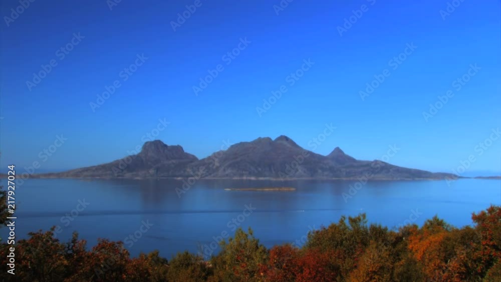 A scenic view of a fjord in Norway with an island in the distance. Leaves of the trees have become red and yellow. A scenic view of a fjord in Norway with an island in the distance. Leaves of the trees have become red and yellow.
