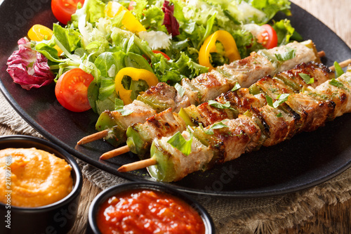 Spicy pork shish kebab with green pepper on skewers with fresh salad on a plate and sauces close-up. horizonta
