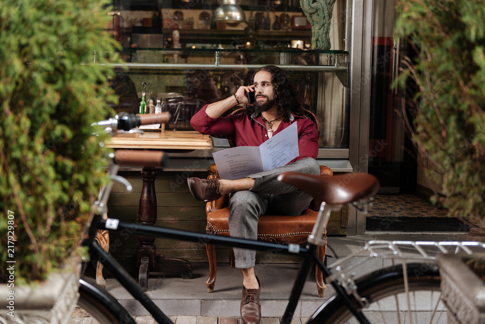 Obraz premium Distance connection. Handsome long haired man making a call while holding the menu in the restaurant
