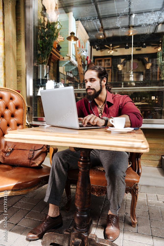 Remote job. Serious bearded man working on a laptop while being a freelancer Remote job. Serious bearded man working on a laptop while being a freelancer