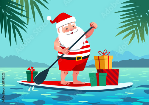 Cute Santa Claus in shorts and t-shirt on a stand up paddle board with gifts, against tropical ocean background with palm trees. Warm weather Christmas celebration, warm climate holiday vacation theme