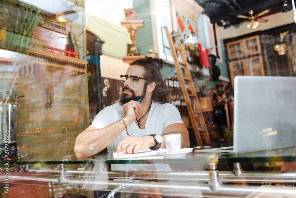 Taking notes. Nice thoughtful man holding a pen while taking notes in the cafe Taking notes. Nice thoughtful man holding a pen while taking notes in the cafe