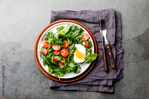 Fresh summer salad with baby spinach, tomatoes cherry and egg. Top view, copy space. Slate gray background photo