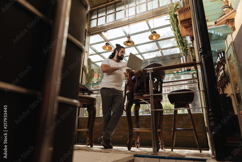 In the bar. Nice handsome man standing in the bar while working on his laptop In the bar. Nice handsome man standing in the bar while working on his laptop