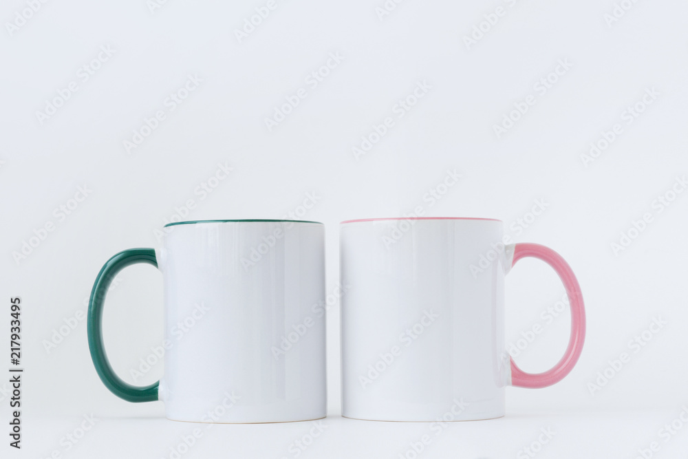 Two white mugs, with a green and pink handle on a light background. Side view. Two white mugs, with a green and pink handle on a light background. Side view.