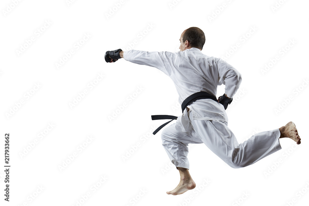 With a black belt, an adult athlete beats with a hand in the jump isolated