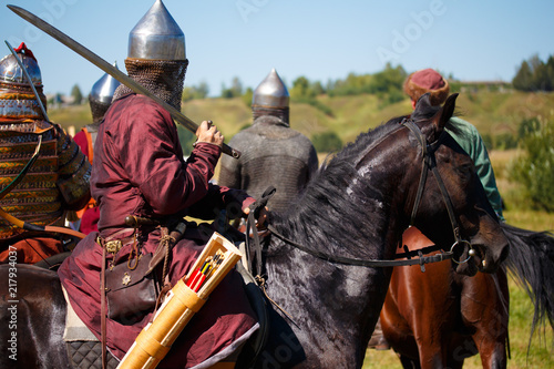 Reconstruction. Medieval armored knight on horse. Equestrian soldier with saber in historical costume. Reenactors