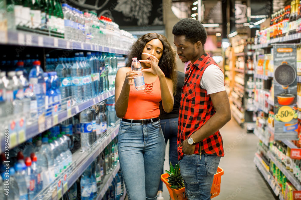 African couple shopping in beverage section at supermarket. Couple doing shopping at market while buying cold drink. Handsome guy holding shopping basket