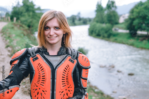 close up portrait of happy girl in body armor with big adventure motorcycle with bags and camping equipment, off road travel jorney, traveling together, couple, mountains dirt road and river © Sergey
