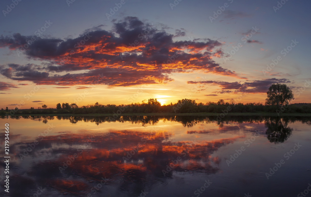 Beautiful colorful summer sunset with amazing sky over river. Pink, yellow and red cloudscape.