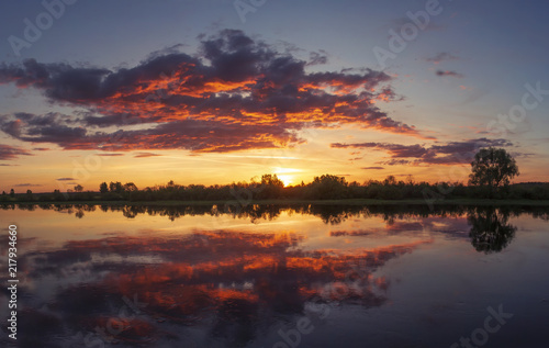 Beautiful colorful summer sunset with amazing sky over river. Pink  yellow and red cloudscape.